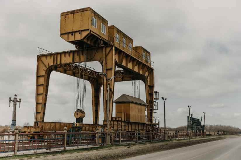 Ilustrasi pelabuhan peti kemas dengan infografis kesalahan fatal dalam desain gantry crane, termasuk masalah struktur, beban, pondasi, dan angin