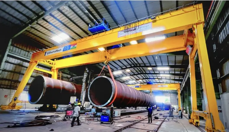 Gantry crane ElectroMech mengangkat komponen silinder berukuran besar di area fabrikasi industri.