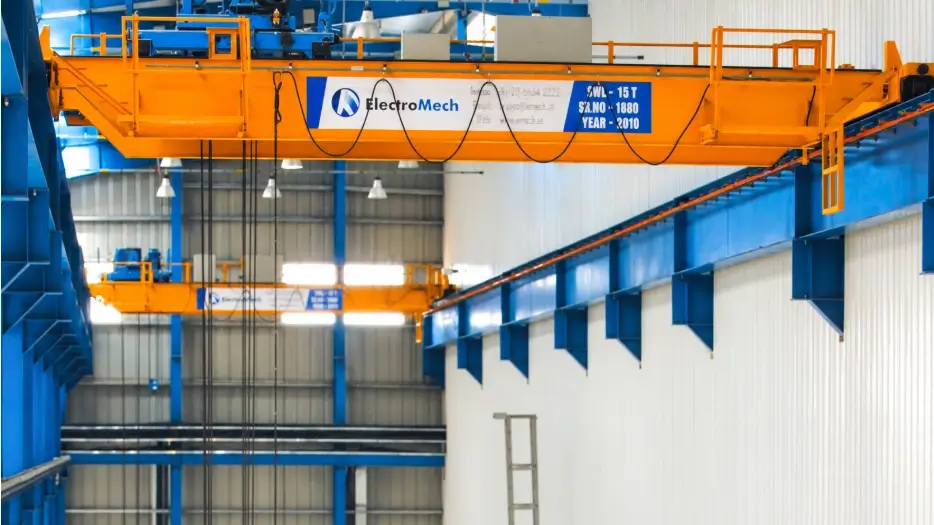 Dua crane ElectroMech berwarna oranye di dalam pabrik, digunakan sebagai visual konsultasi pencegahan shock load crane.