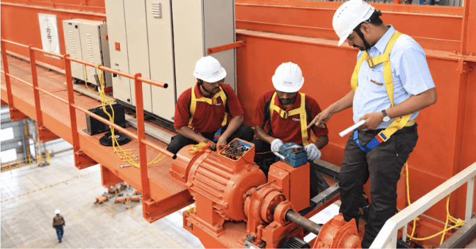 Tiga teknisi memeriksa motor dan komponen penggerak crane sebagai ilustrasi biaya perawatan dalam perhitungan TCO hoist crane.