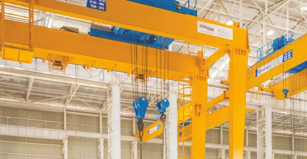 Crane ElectroMech membentang di atas deretan dies dan mould, dengan trolley hoist serta jalur hijau di tengah tool room.